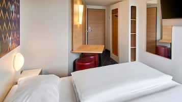 A hotel room with a bed, a desk, a chair, a wardrobe, and a mirror.