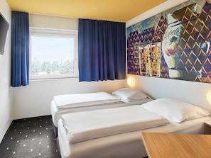 A hotel room with two beds, a window with curtains, a wall-mounted light, and a city view. - B&B Hotel Frankfurt-Nord (Frankfurt)