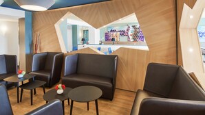 A modern lounge area with leather sofas and tables, a reception desk, and a wooden accent wall.