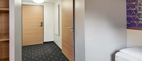 A hotel room with a bed, a wardrobe, and a hallway with a patterned carpet.