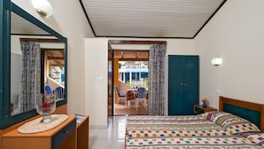 A hotel room with a bed, a desk, a mirror, a wardrobe, and a view of the outside patio.