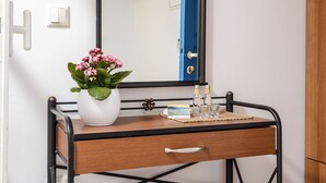 A compact room with a wooden desk, a mirror, a television mounted above, and a small stool. - Studios Diogenis (Naxos)