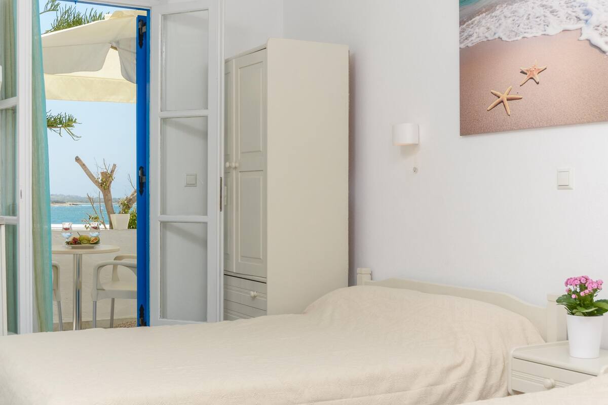 A bedroom with a bed, a nightstand, a potted plant, and a painting of a beach scene.