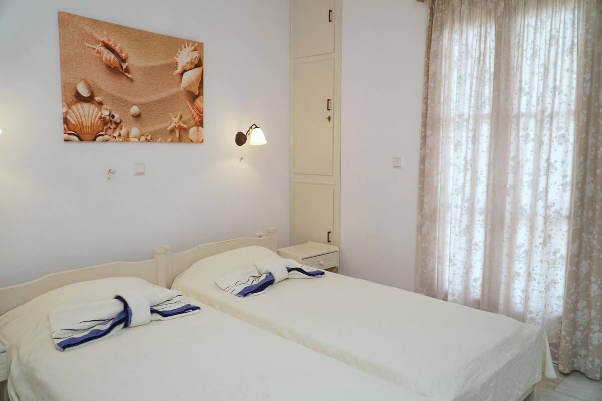 A hotel room with two beds, a large seashell wall art, a nightstand, a mirror, and a floral curtain.