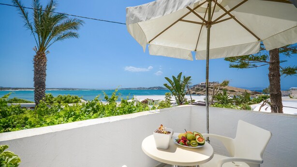 A balcony with a white table, two white chairs, a white umbrella, and a fruit plate. - Studios Diogenis (Naxos)