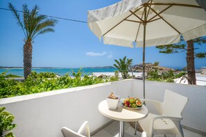 Een balkon met een witte tafel, twee witte stoelen, een witte parasol en een schaal met fruit.