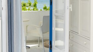 An open door leading to a balcony with a view of the sea, a white chair, and a white cabinet. - Studios Diogenis (Naxos)