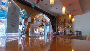A bar area with a polished wooden counter, a coffee sign, and shelves stocked with bottles. - Silver Beach Hotel and Annexe Apartments (Corfu)