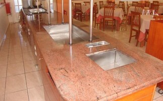 Una cocina con encimeras de granito, lavamanos de acero inoxidable y sillas de madera.