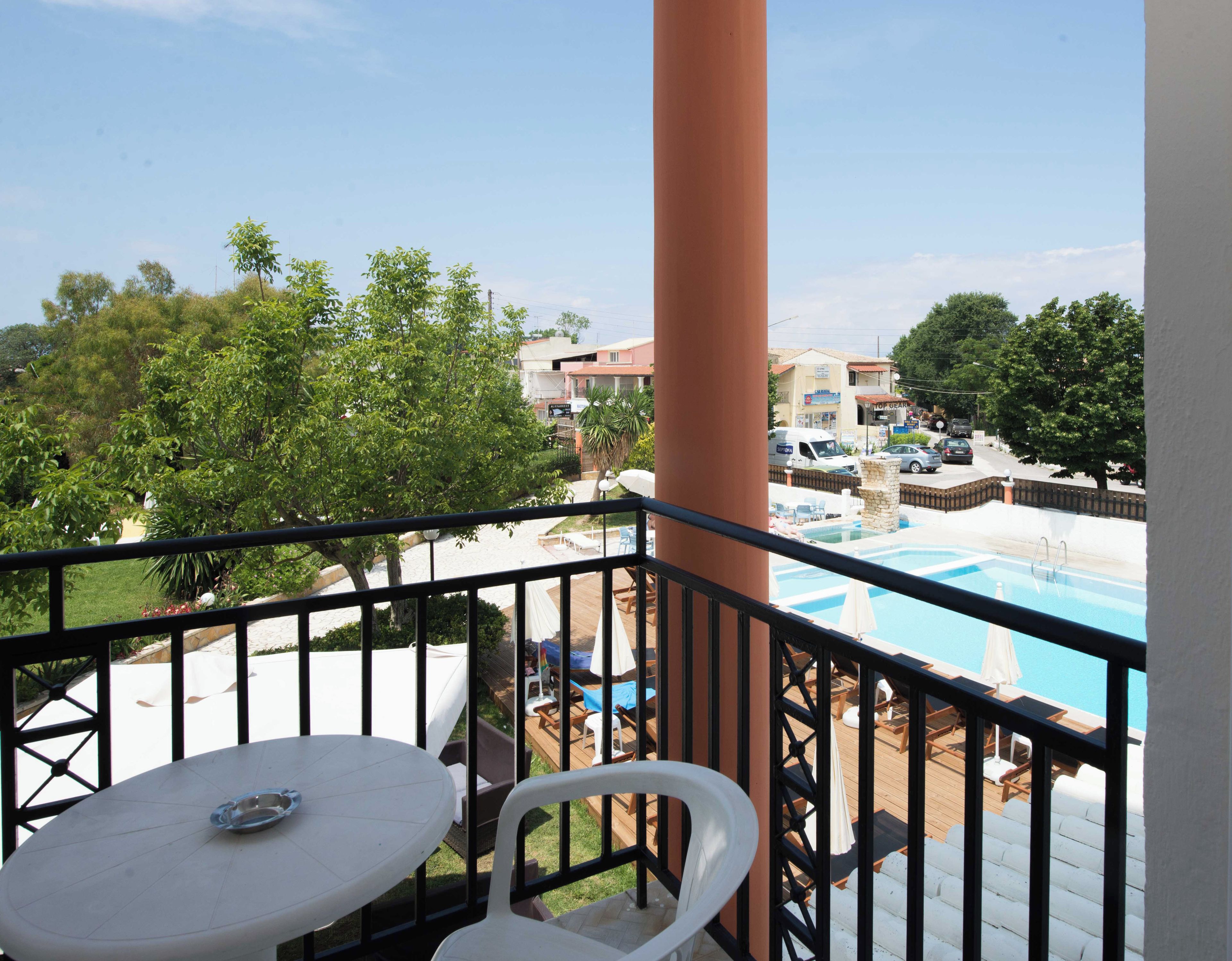 A balcony with a view of a swimming pool, outdoor furniture, and a building in the background.