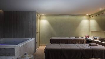 A spa room with a massage table, a bathtub, and a large mirror.