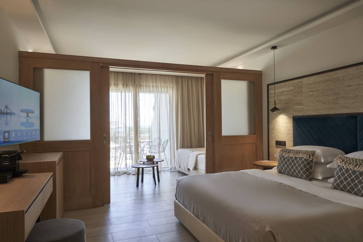 A hotel room with a bed, a desk, a chair, a TV, and a balcony with curtains.