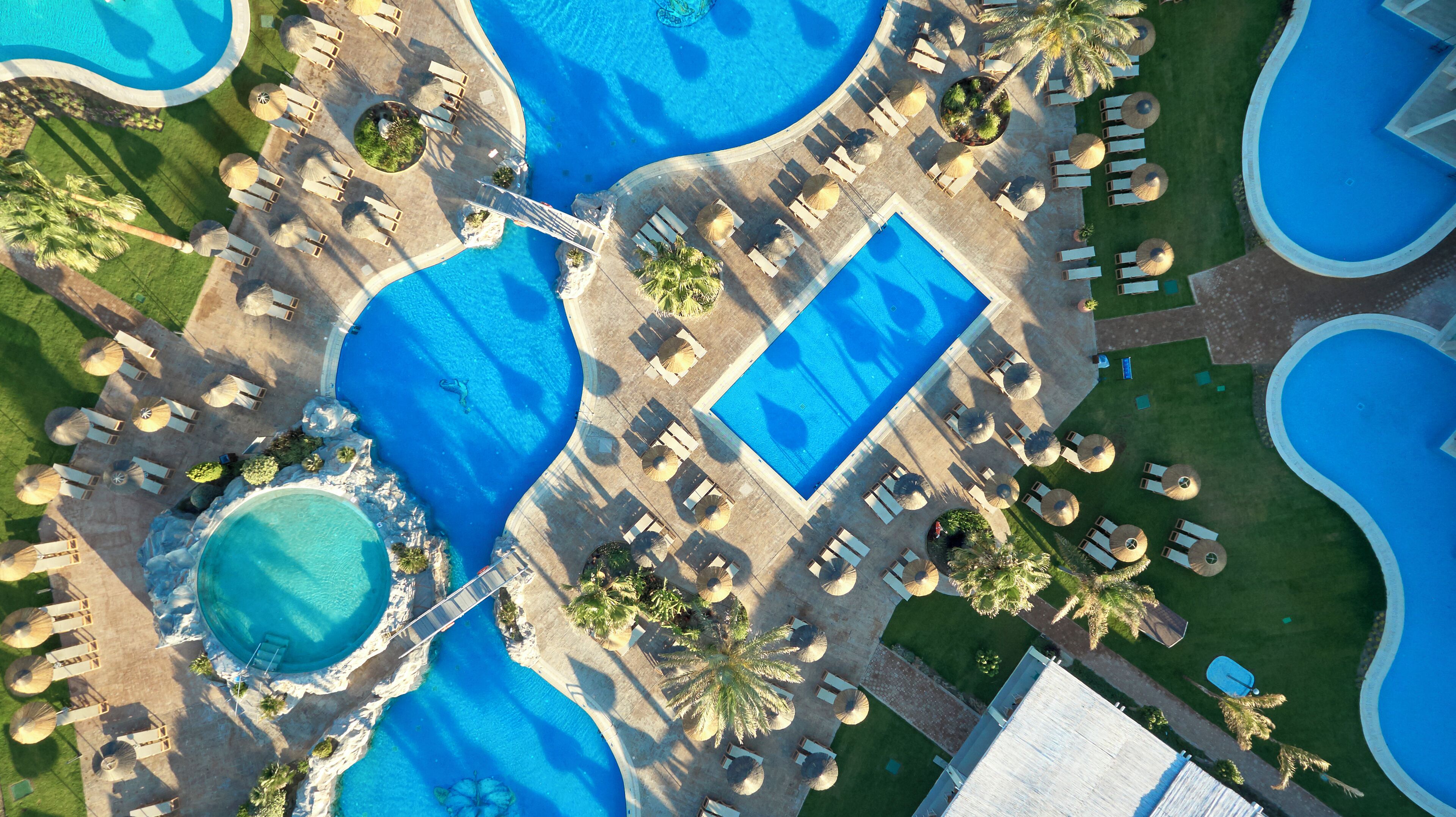 An aerial view of a resort with multiple swimming pools, sun loungers, and palm trees.