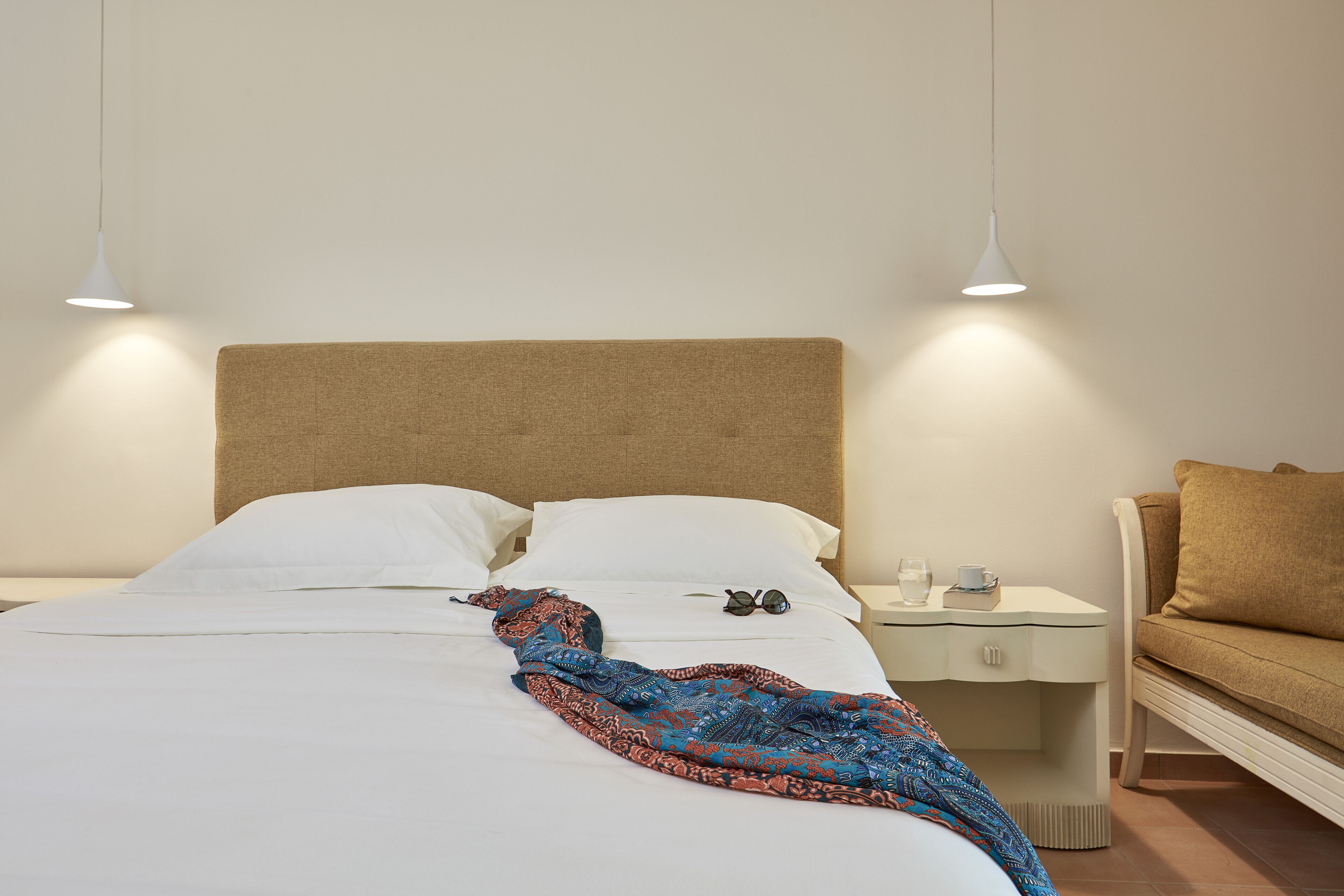 Un lit bien fait, avec des draps blancs, une couverture à motifs et une paire de lunettes de soleil posée sur la table de chevet.