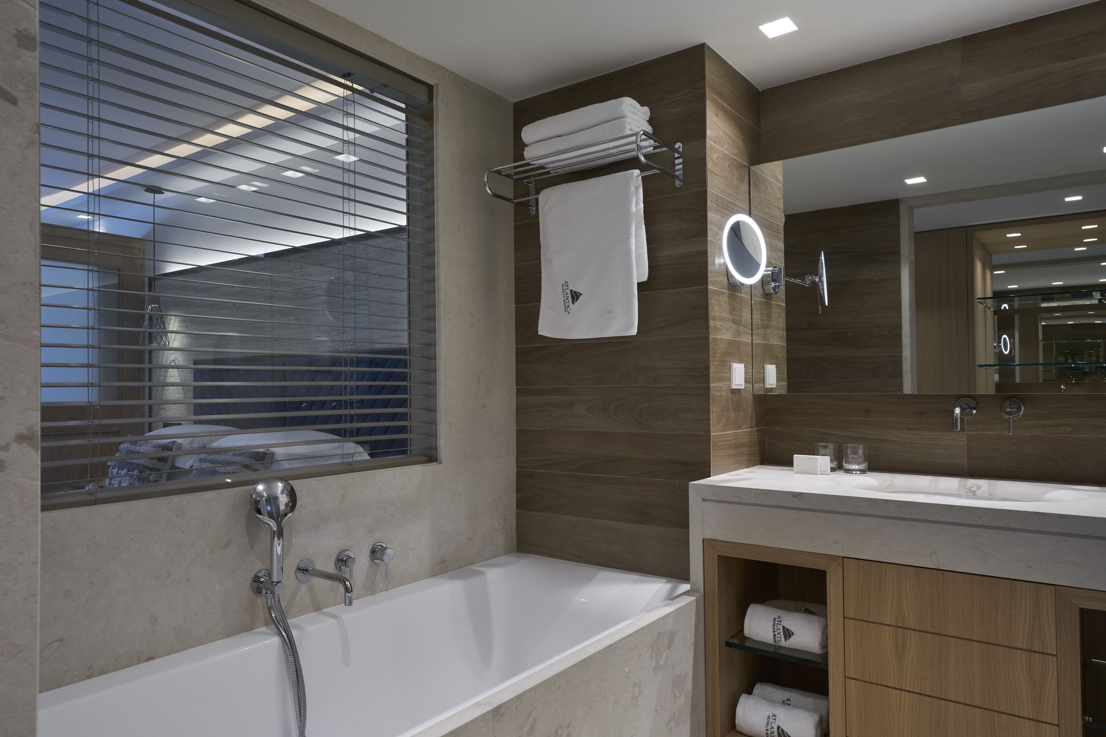 A modern bathroom with a bathtub, a large mirror, and wooden cabinetry.