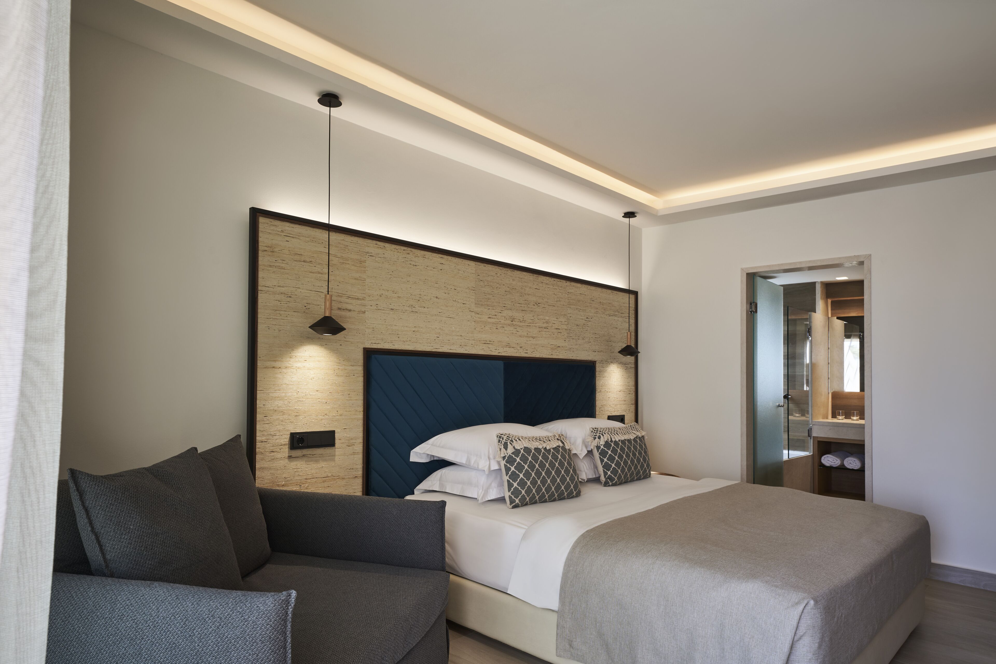 A modern hotel room with a large bed, a sofa, a wooden accent wall, and a mirror.