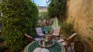 A cozy outdoor seating area with a round table, chairs, and a potted plant. - Riad Norma (Fes)