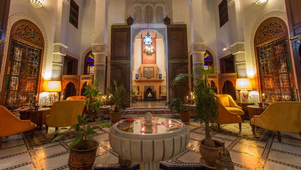 A lobby with a central fireplace, ornate arches, and seating areas with potted plants. - Riad Norma (Fes)