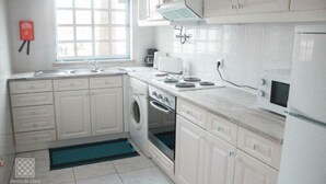 A modern kitchen with white cabinets, a built-in oven, a microwave, and a washing machine. - Sereia da Oura (Albufeira)