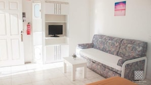 A room with a white sofa, a small white table, and a television on a white cabinet. - Sereia da Oura (Albufeira)