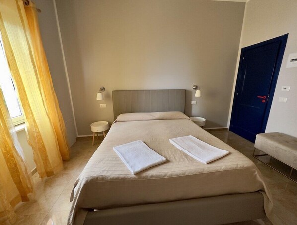 A hotel room with a large bed, two bedside tables, a blue door, and a window with curtains. - Inn Piero (Taormina)