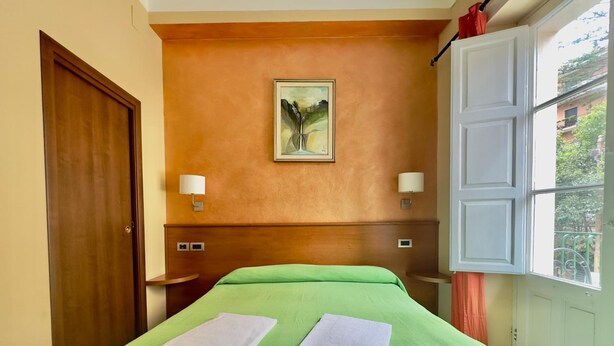 A hotel room with a green bedspread, two towels, a painting on the wall, and a window with a view. - Inn Piero (Taormina)