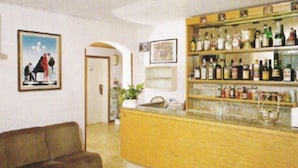 A bar area with shelves of bottles and glasses, a brown couch, and framed pictures on the walls. - Abay (Rimini)