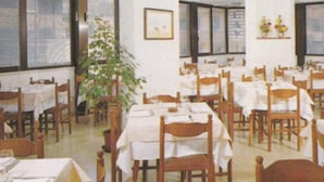 A dining area with multiple tables and chairs, large windows, and a potted plant. - Abay (Rimini)