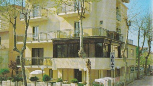 A multi-story yellow building with balconies, a covered outdoor seating area, and a sign reading "ABAY". - Abay (Rimini)