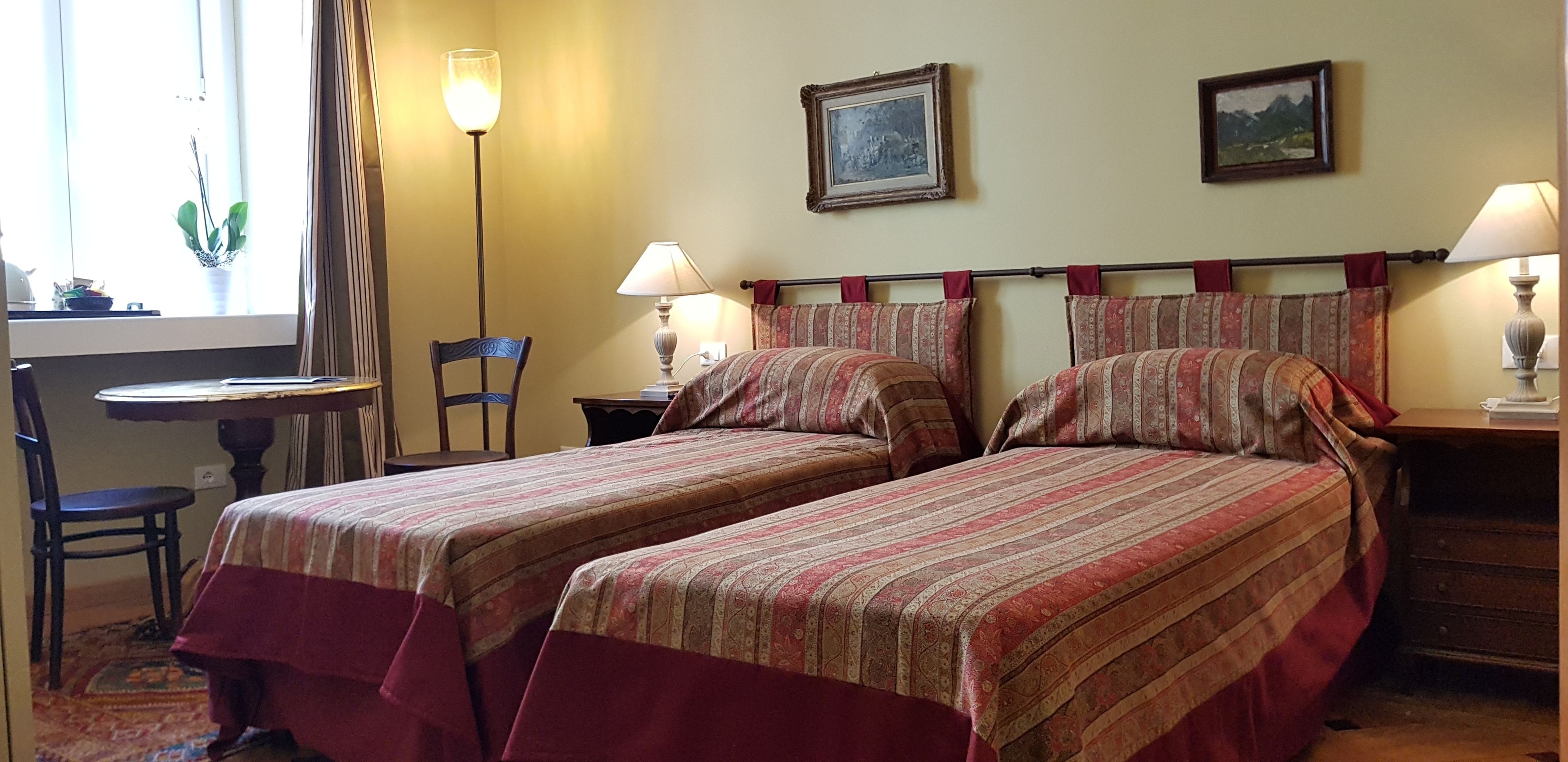 Une chambre avec deux lits, une chaise, une petite table et deux lampes.