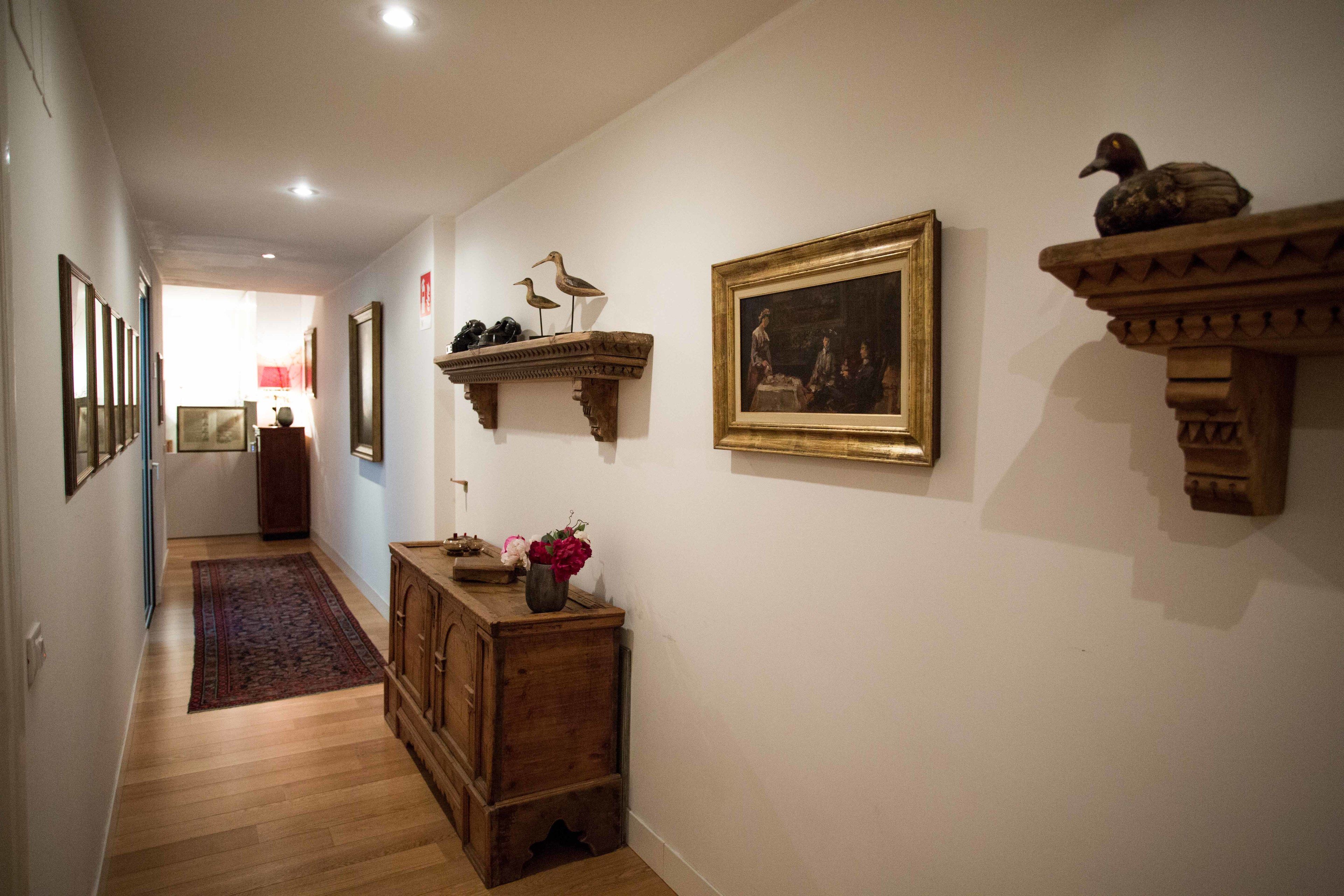 A hallway with wooden flooring, a wooden cabinet, a rug, and wall-mounted decorations including a framed painting and two bird sculptures.