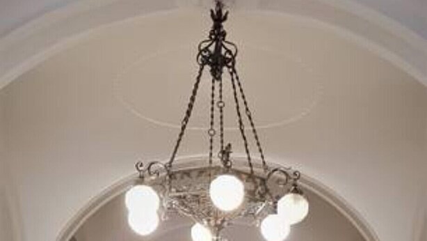 An arched hallway with a patterned floor, a chandelier, and a large door with glass panels. - Residenza Le 6 A (Trieste)