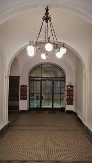 Un pasillo abovedado con piso estampado, un candelabro y una puerta grande con paneles de vidrio.