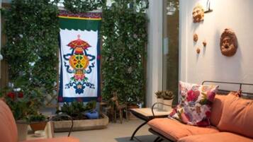 A cozy outdoor seating area with a cushioned sofa and a table, surrounded by potted plants and a decorative banner.