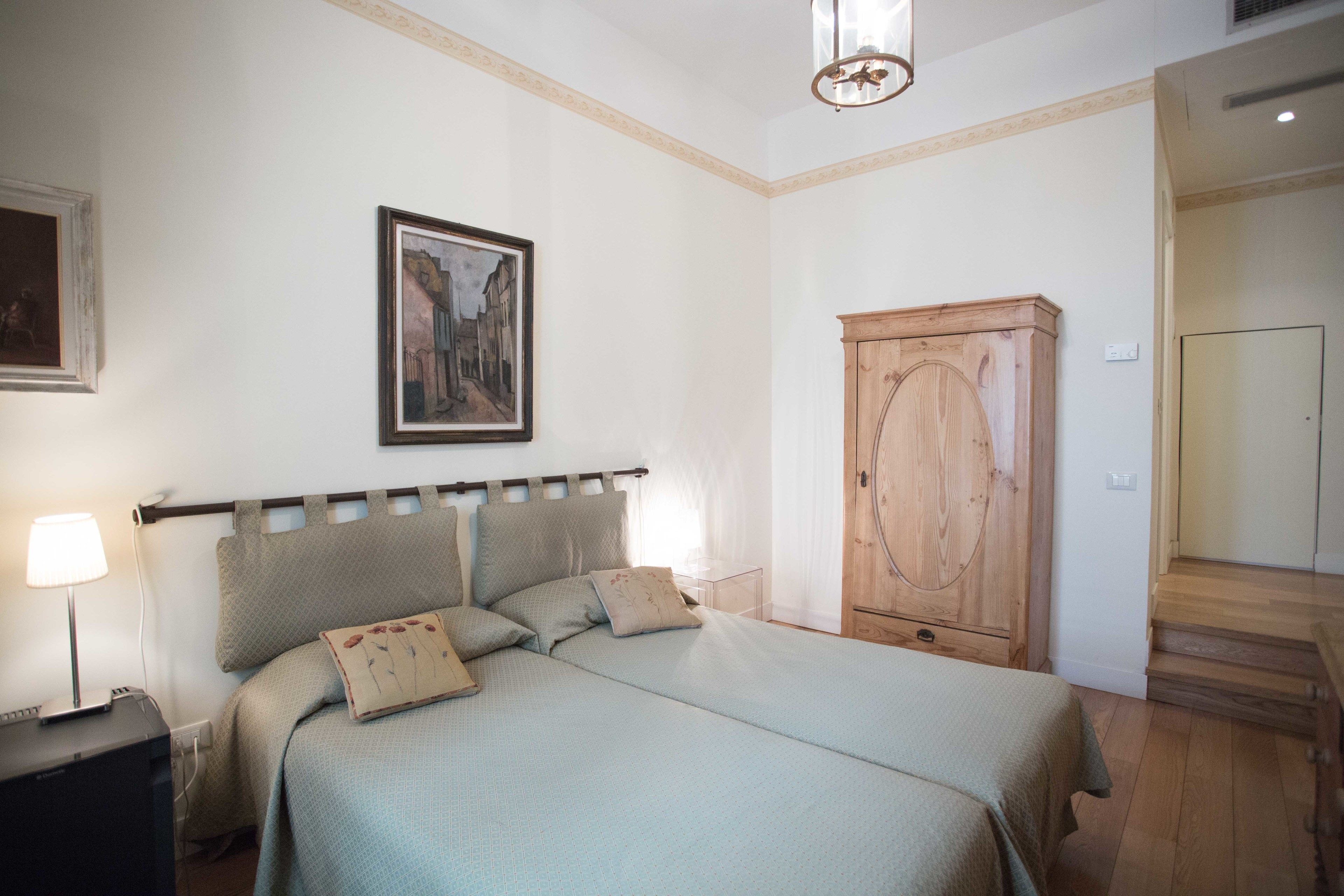 Un dormitorio con cama, mesita de noche, lámpara, armario de madera y un cuadro en la pared.