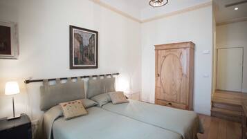 Un dormitorio con cama, mesita de noche, lámpara, armario de madera y un cuadro en la pared.