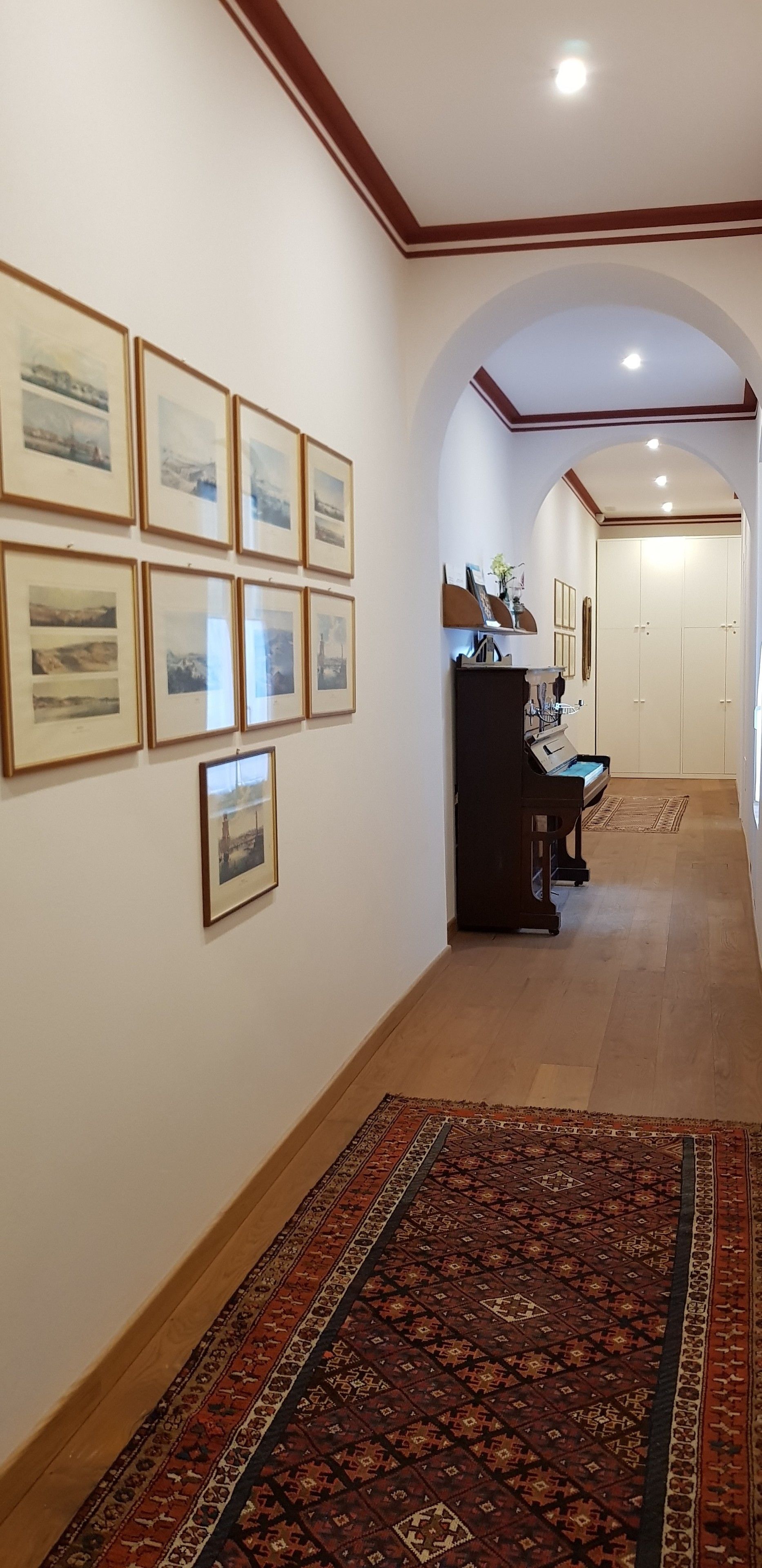 A hallway with framed pictures on the wall, a piano, and a carpet.