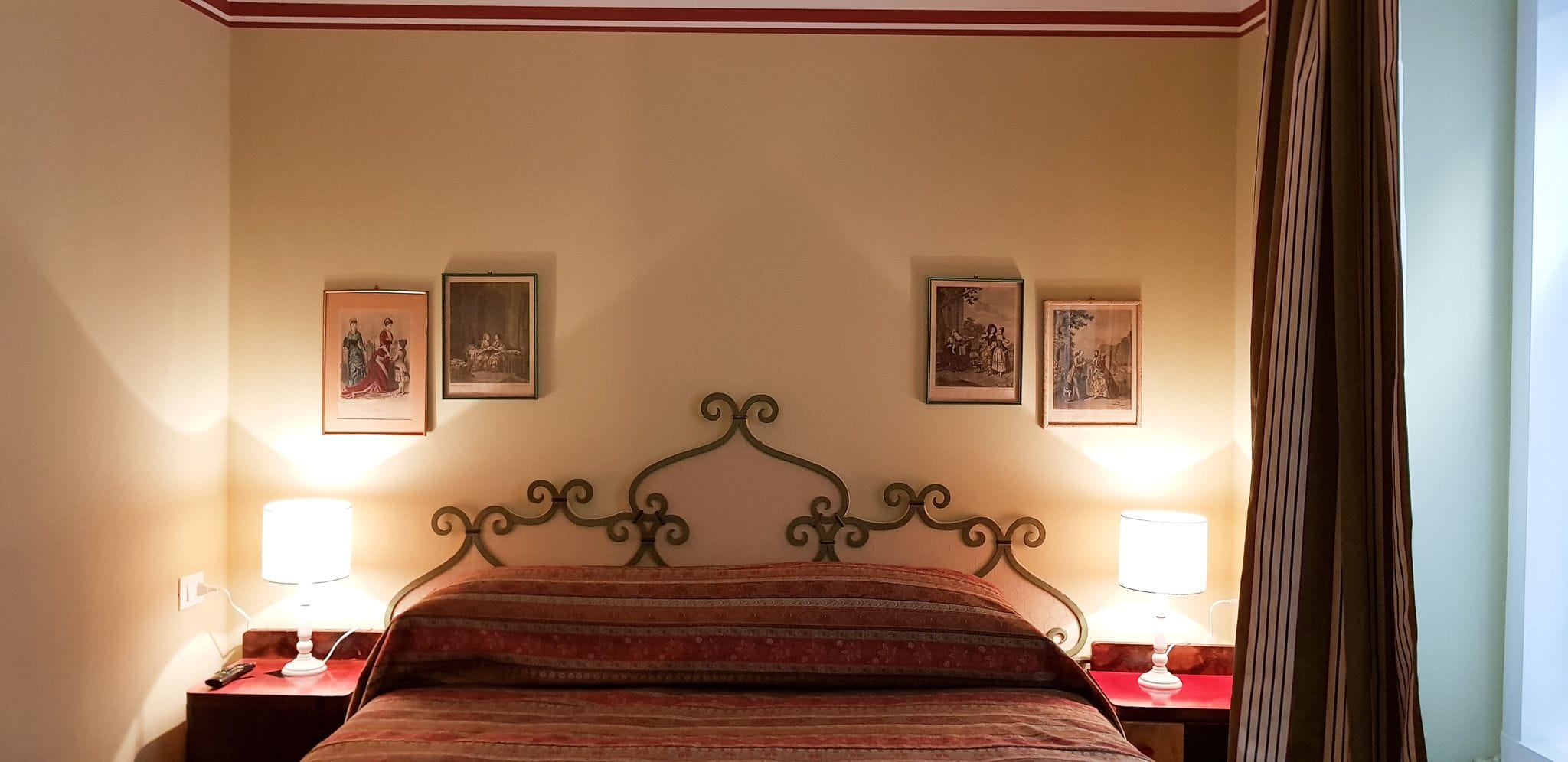 Una habitación de hotel con una cama con dosel, dos mesitas de noche con lámparas y tres cuadros enmarcados en la pared.