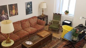 A living room with a sofa, two chairs, a coffee table, a desk with a computer, and a window with a plant.