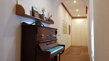 Un pasillo con un piano, una estantería, cuadros enmarcados y una puerta.