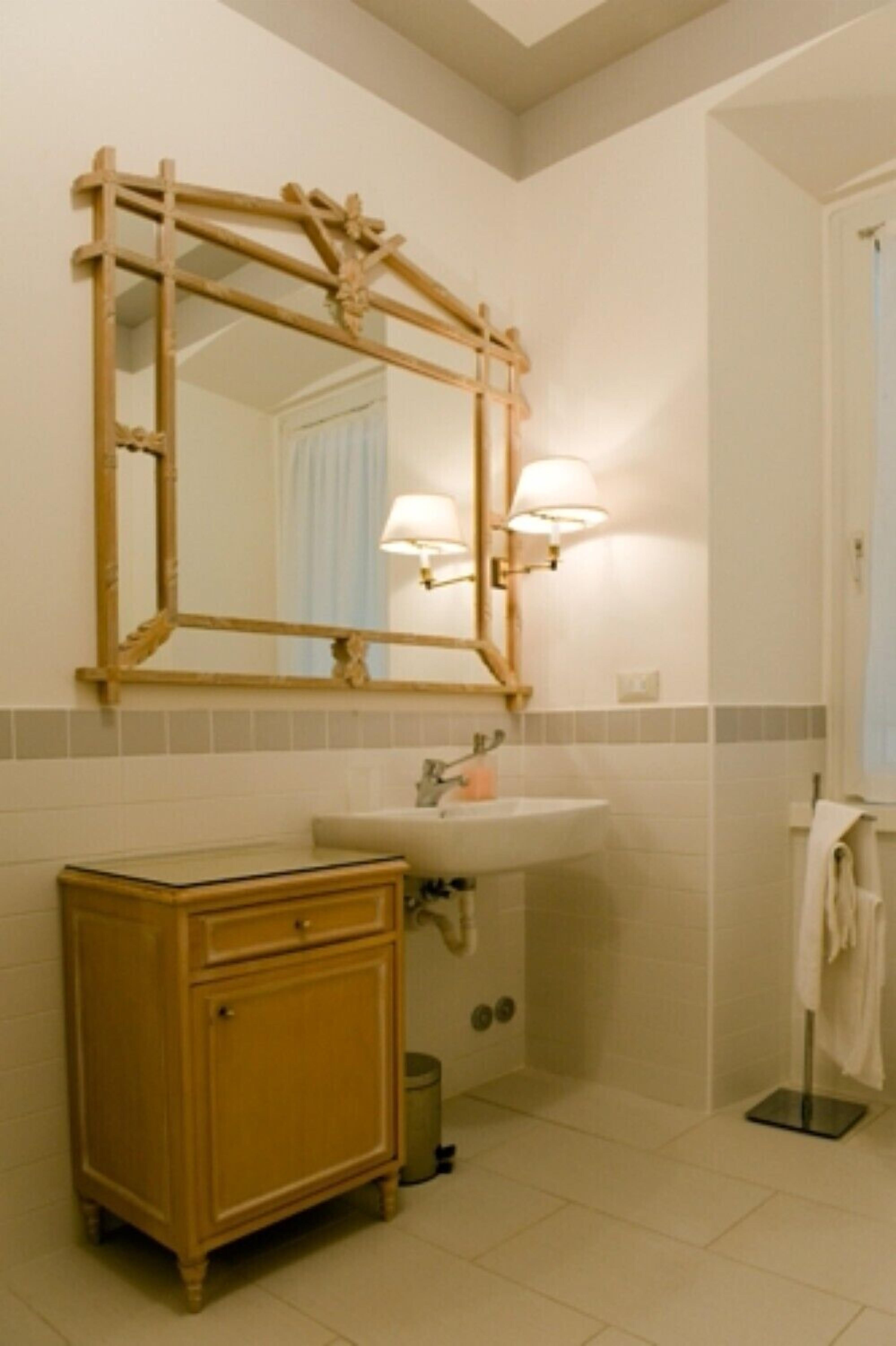 A bathroom with a wooden vanity, a sink with a mirror above it, and two wall-mounted lights.