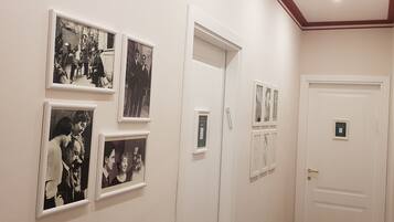 A hallway with framed black and white photographs on the walls, a white door with a keycard slot, and a doorbell.