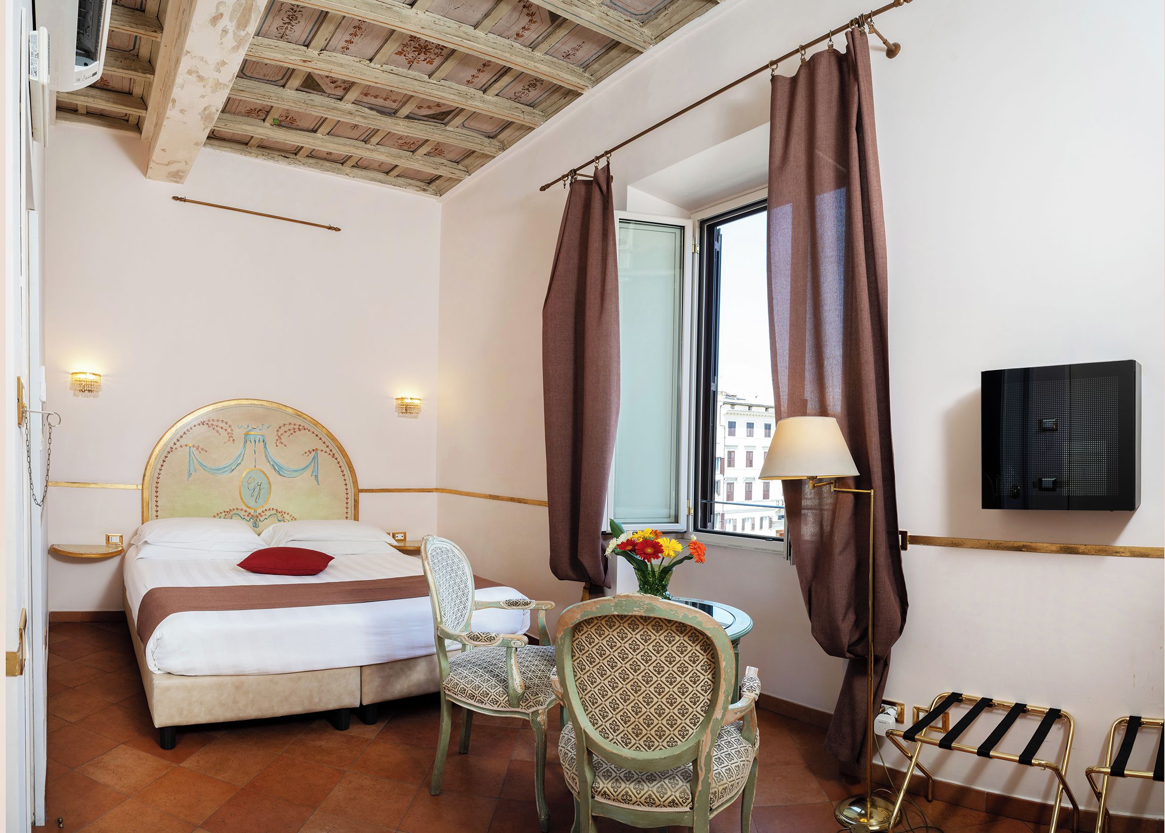 Habitación de hotel con cama, escritorio, silla, televisión y ventana con cortinas.