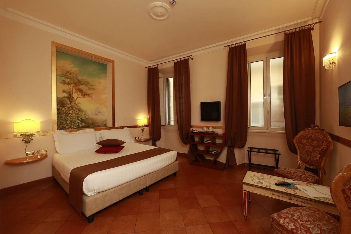 A hotel room with a bed, a desk, a chair, a TV, and a painting on the wall.