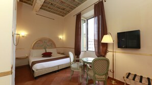 A hotel room with a bed, two chairs, a table, a lamp, a TV, and a window with curtains. - Residenza Gens Julia (Rome)