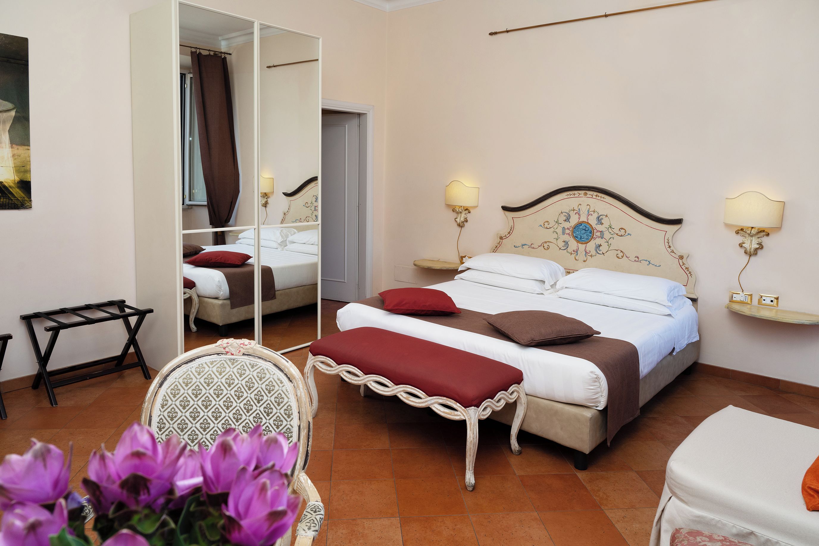 Habitación de hotel con una cama grande, dos lámparas de noche, un espejo, una mesita y una silla.