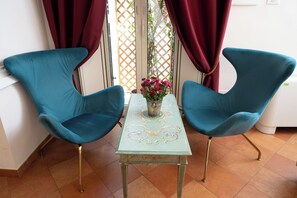 Two teal chairs with gold legs, a small table with a floral pattern, and a vase with pink flowers. - Residenza Gens Julia (Rome)