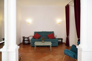 A living room with a teal sofa, two red cushions, a small table with a flower vase, and a blue armchair. - Residenza Gens Julia (Rome)