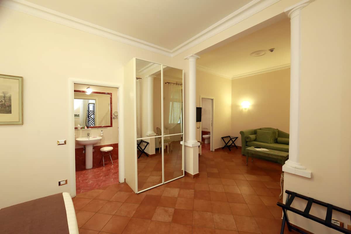 A spacious living area with a green sofa, a dining table, and a mirrored wall leading to a bathroom.