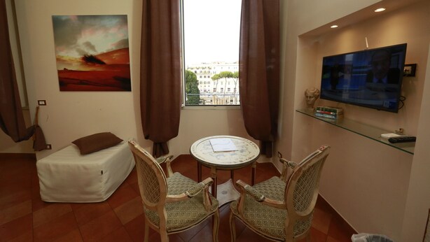 A small living area with a sofa, two chairs, a table, a painting, a TV, and a window with curtains. - Residenza Gens Julia (Rome)